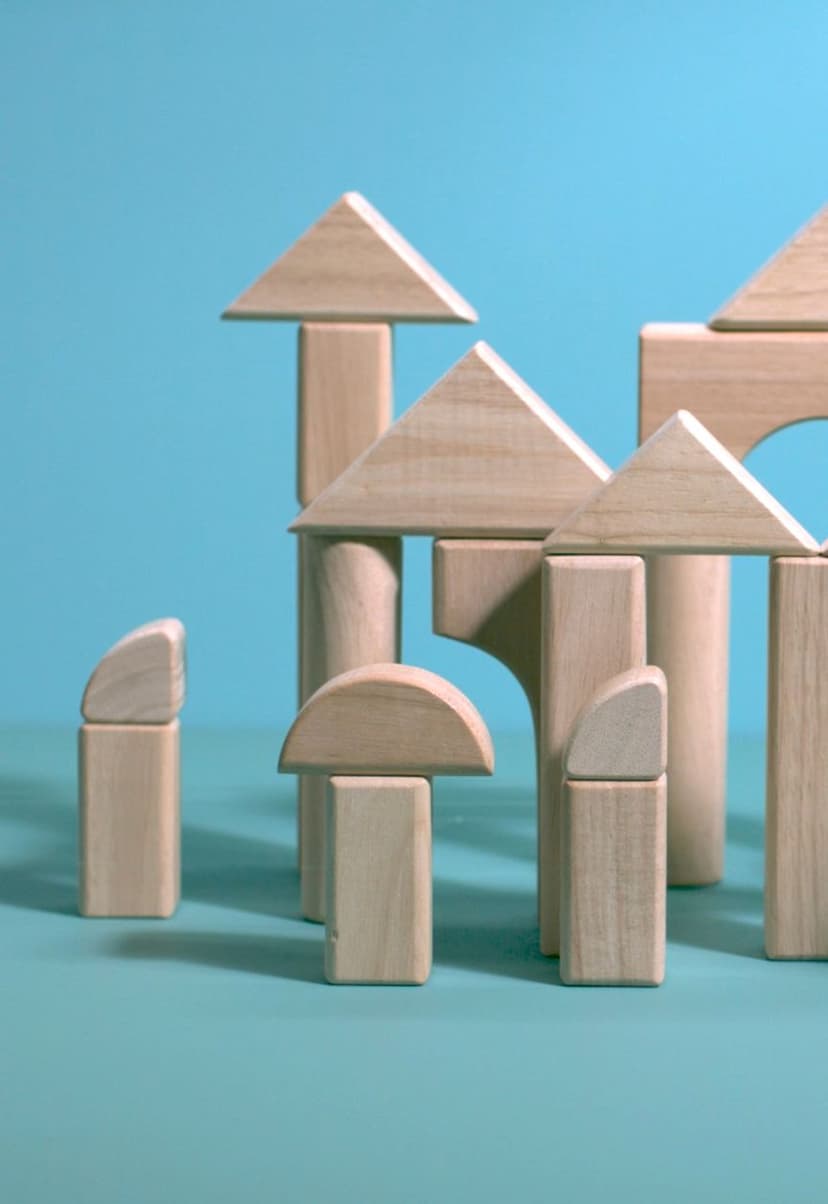 Wooden building blocks arranged to resemble small houses and structures on a teal surface with a blue background.